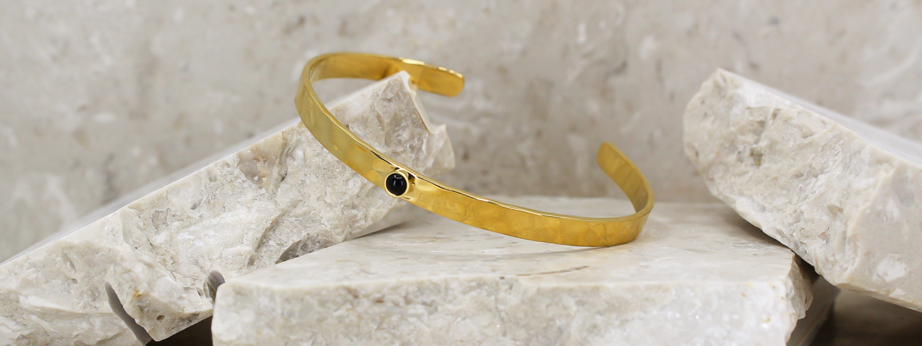Header bild för kategorin armband. Golden black stone bracelet i en  produktbild med stenar som bakgrund
