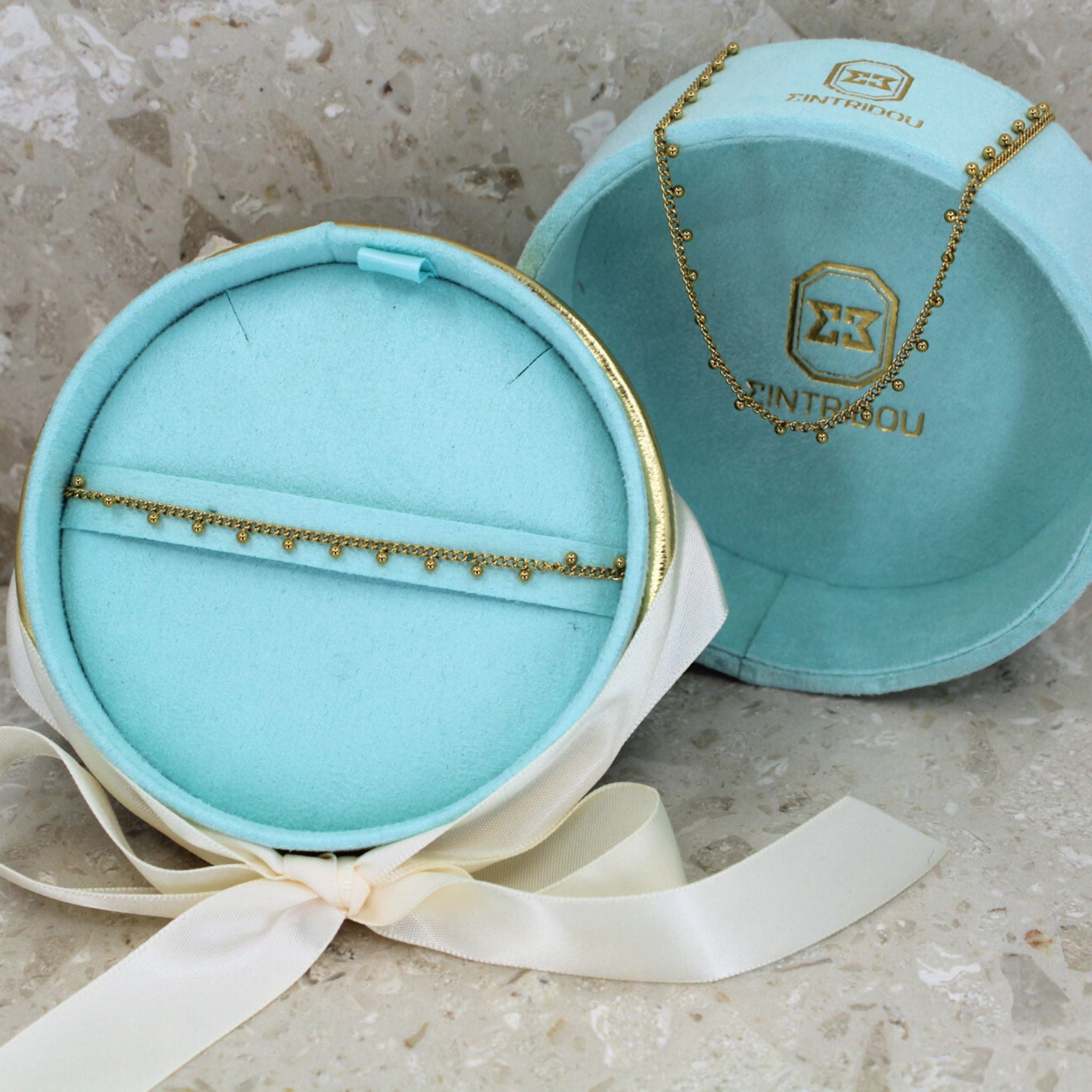 Ett smyckeset med golden beaded halsband och armband i 18k guld plätering, i en turkos sammet presentask